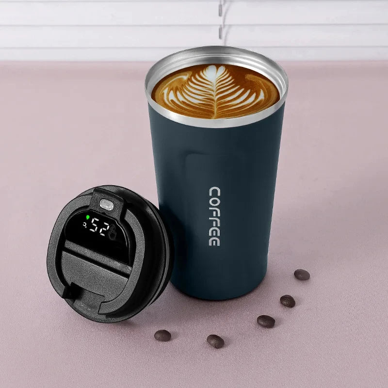 Blue insulated coffee cup with a digital temperature display lid, surrounded by coffee beans on a light pink background.