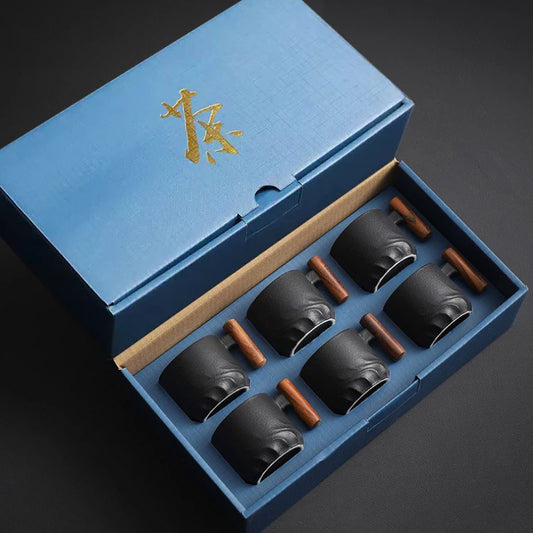 Set of black ceramic cups with wooden handles in a blue box on a dark background