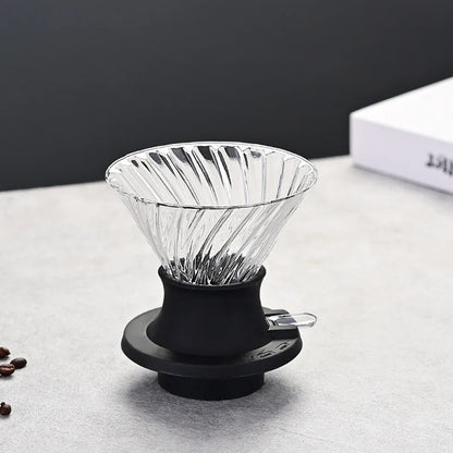 Clear glass coffee dripper with black rubber collar on a light gray surface.