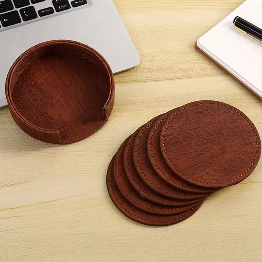 Set of brown leather coasters on a wooden surface with a laptop in the background.