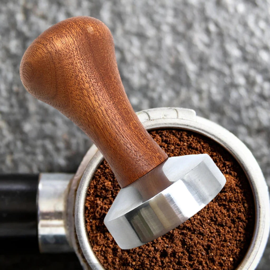 Wooden handle coffee tamp pressing down on coffee grounds in a portafilter.