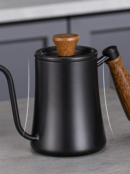 Matte black gooseneck kettle with a wooden handle and wooden lid knob, shown on a gray countertop with a blurred kitchen background.