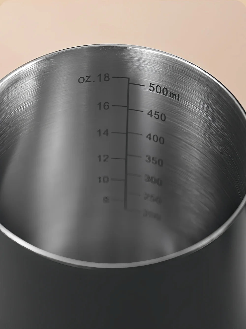 Close-up of the inside of a brushed stainless steel measuring pitcher or mixing bowl with printed liquid level markings in ounces and milliliters.