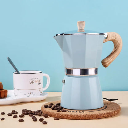 Light blue espresso maker with wooden handle on a cork trivet against a light blue background.