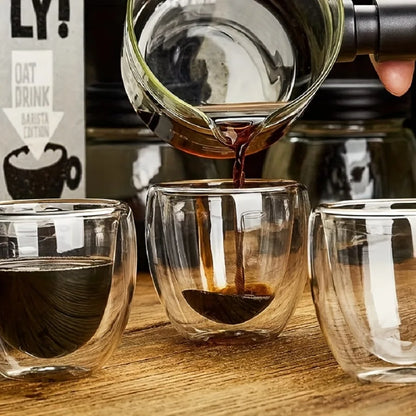 Oat drink being poured from a bottle into two glass cups on a wooden surface.