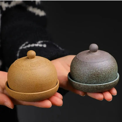 Two ceramic containers with lids held in hands against a dark background