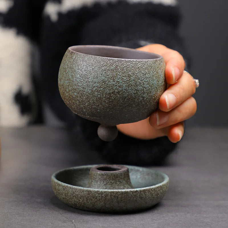 Hand holding a textured ceramic cup with matching saucer on a dark surface