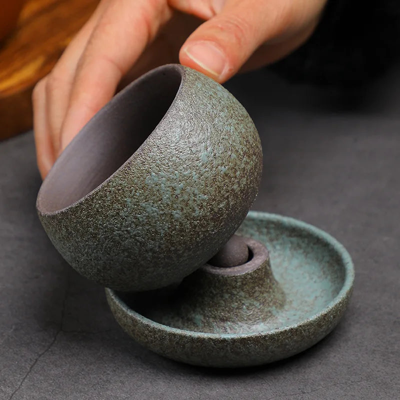 Ceramic tea bowl and saucer set on a dark surface with a hand holding the bowl.