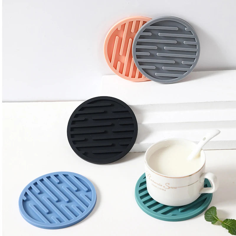 Set of silicone coasters in black, blue, orange, and gray on a white surface with a cup.