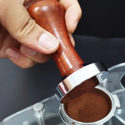Hand using a wooden coffee tamper to compress coffee grounds in a filter basket.