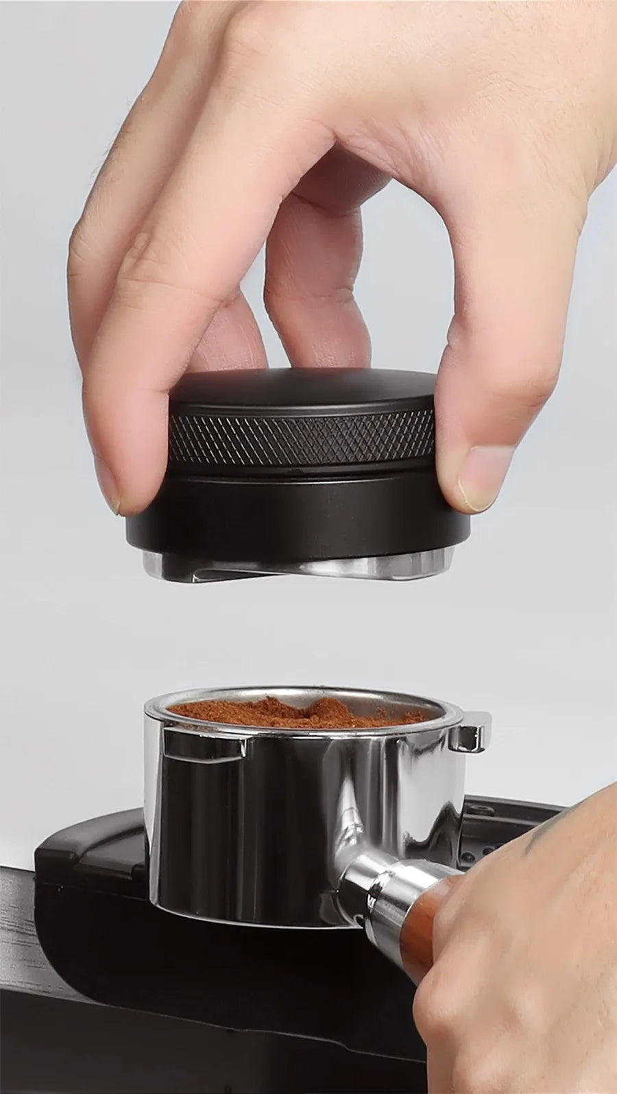 Hand using a coffee tamp to compress coffee grounds into a portafilter.