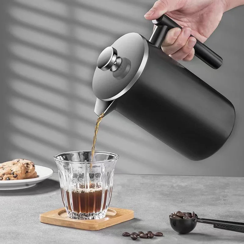 Person pouring coffee from a black French press into a glass cup on a gray surface.