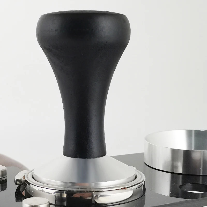 Coffee tamp with black handle and silver base on a reflective surface