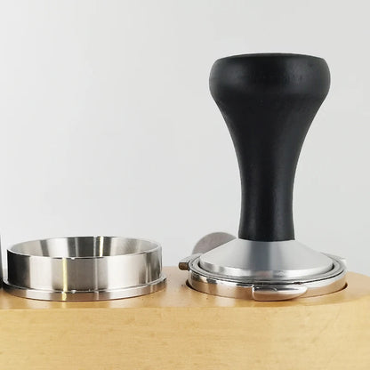 Coffee tamp with black handle and metal base on a light wooden surface.