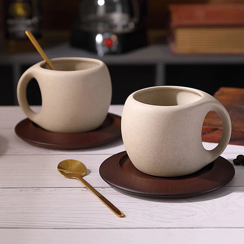 Two ceramic mugs with handles on brown saucers on a wooden surface.