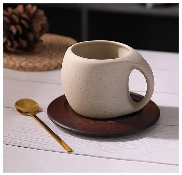 Ceramic mug with handle on a wooden coaster with a gold spoon on a white surface.
