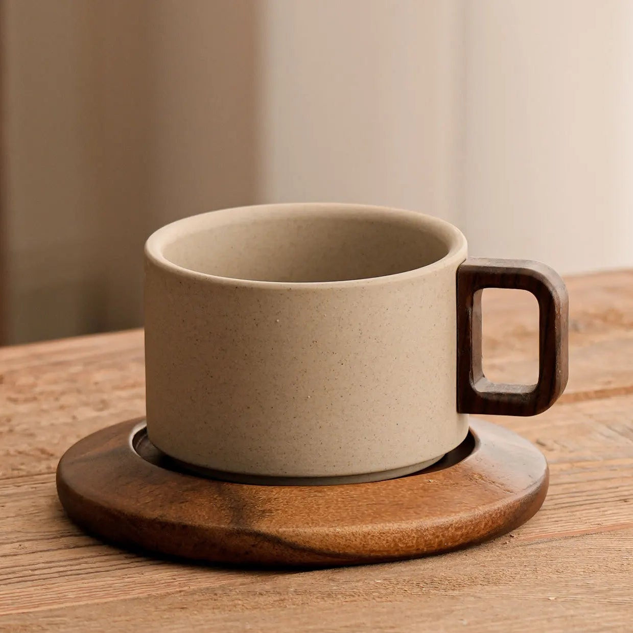 Ceramic mug with wooden handle on a wooden coaster against a neutral background