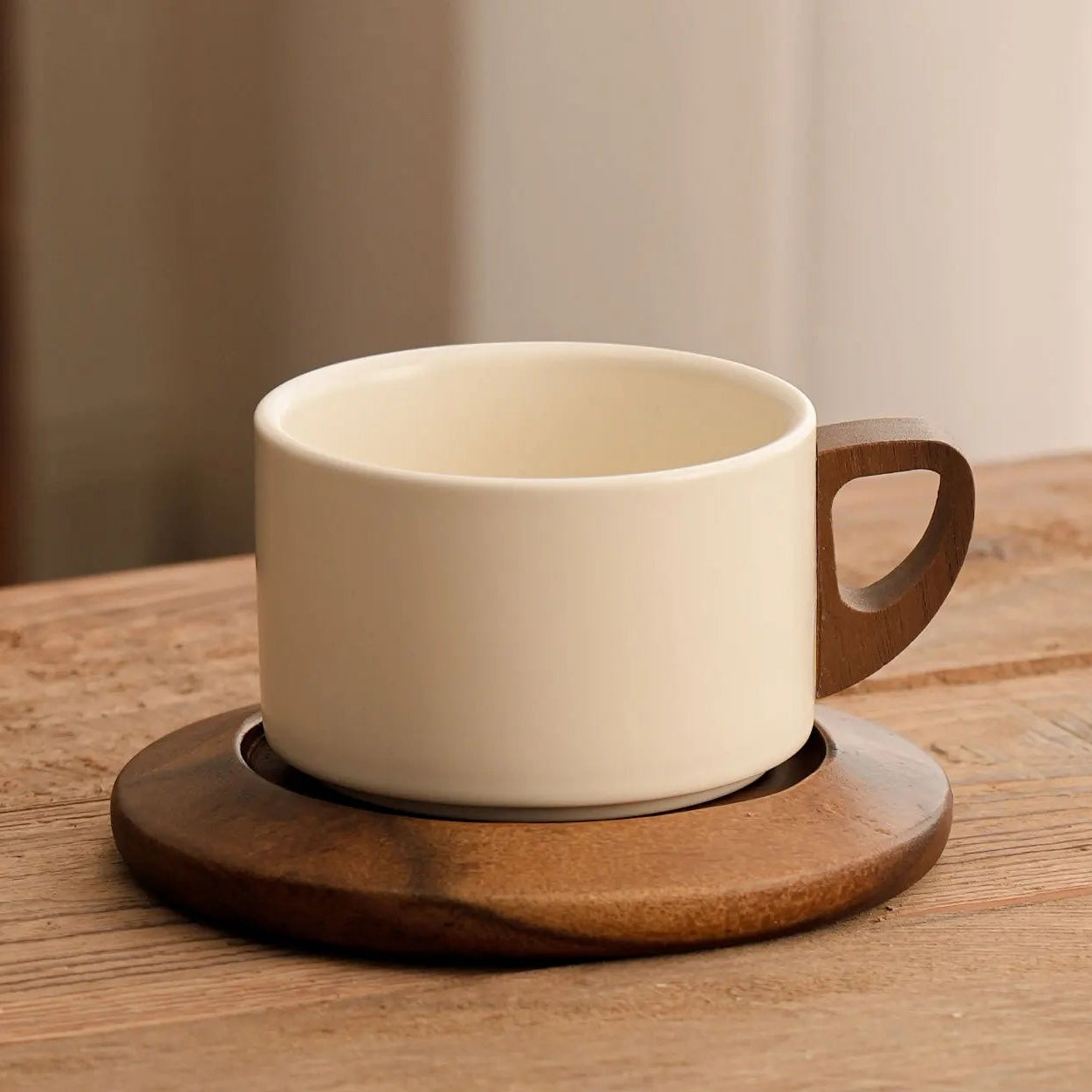 White ceramic coffee cup with wooden handle on a matching coaster on a wooden table.