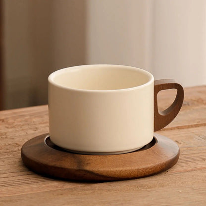 White ceramic coffee cup with wooden handle on a matching coaster on a wooden table.