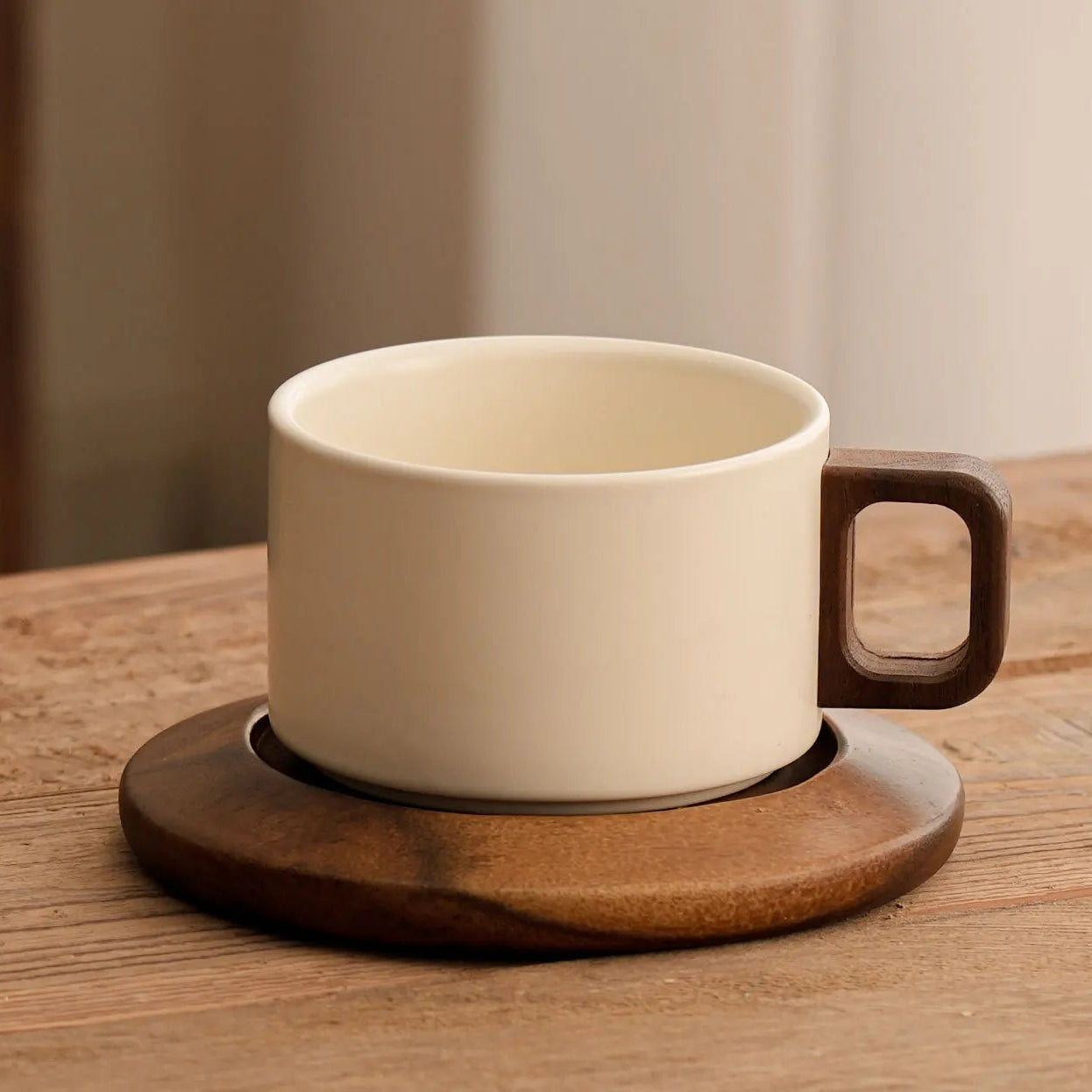 White ceramic coffee cup with wooden handle on a wooden coaster on a wooden table.