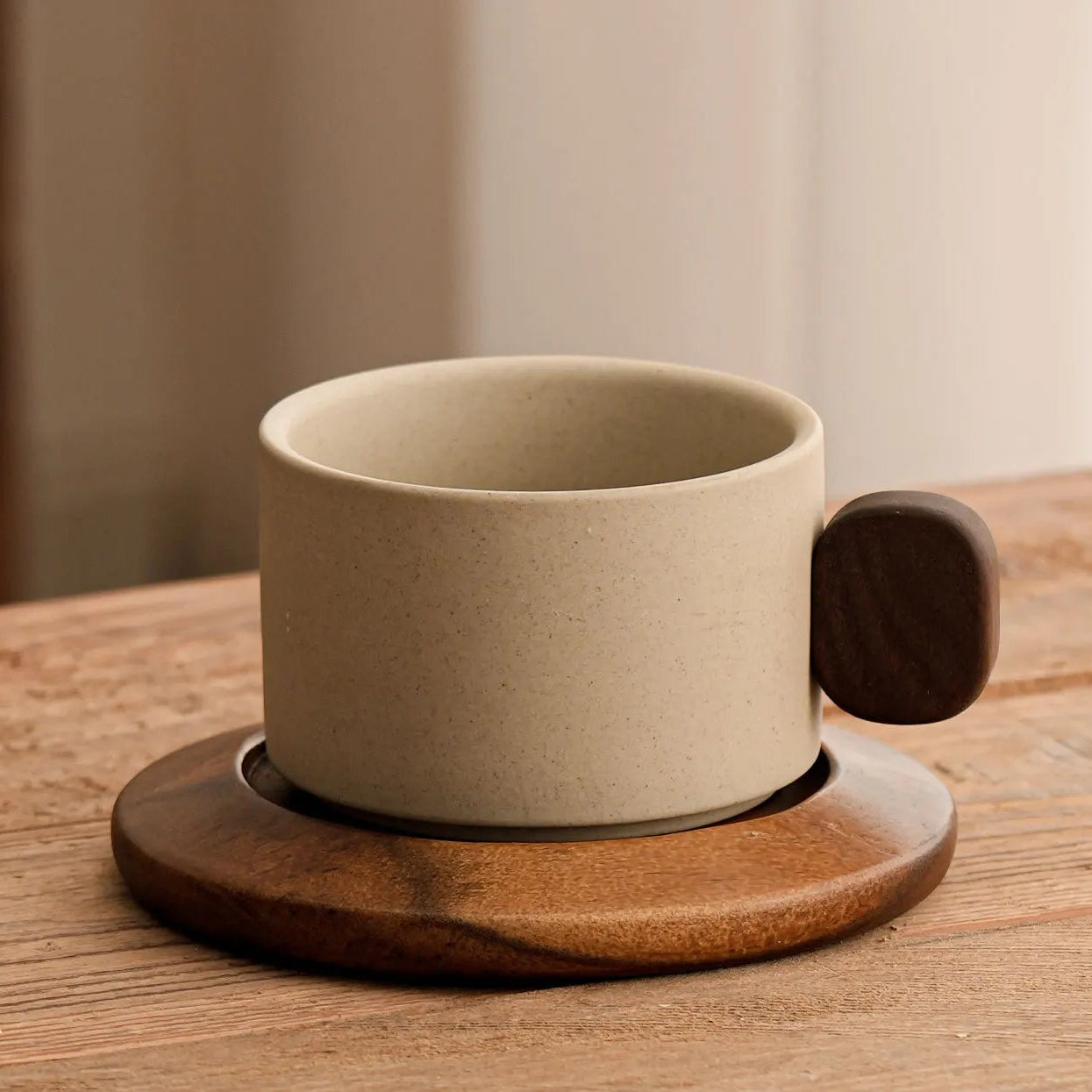Beige ceramic coffee cup with wooden handle and coaster on a wooden surface