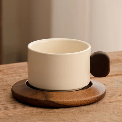 White ceramic coffee cup with wooden handle and coaster on a wooden surface