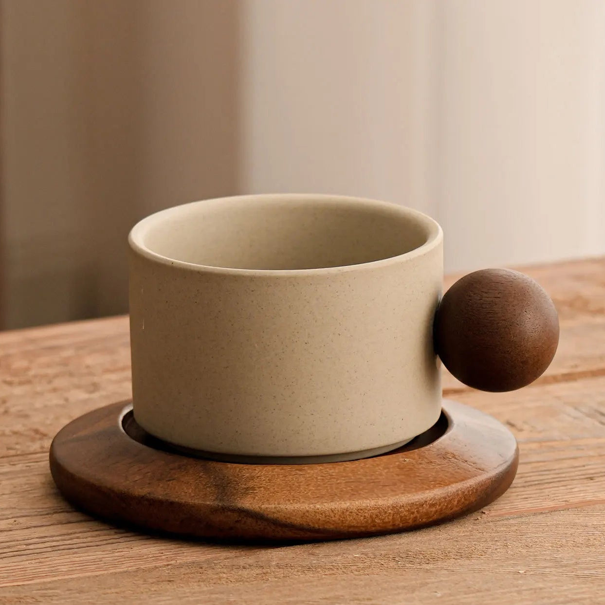 Beige ceramic coffee cup with wooden handle and coaster on a wooden table