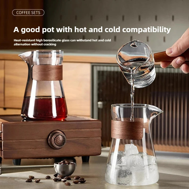 Glass coffee pot with wooden handle being filled with hot water, surrounded by coffee beans and a wooden coffee maker.