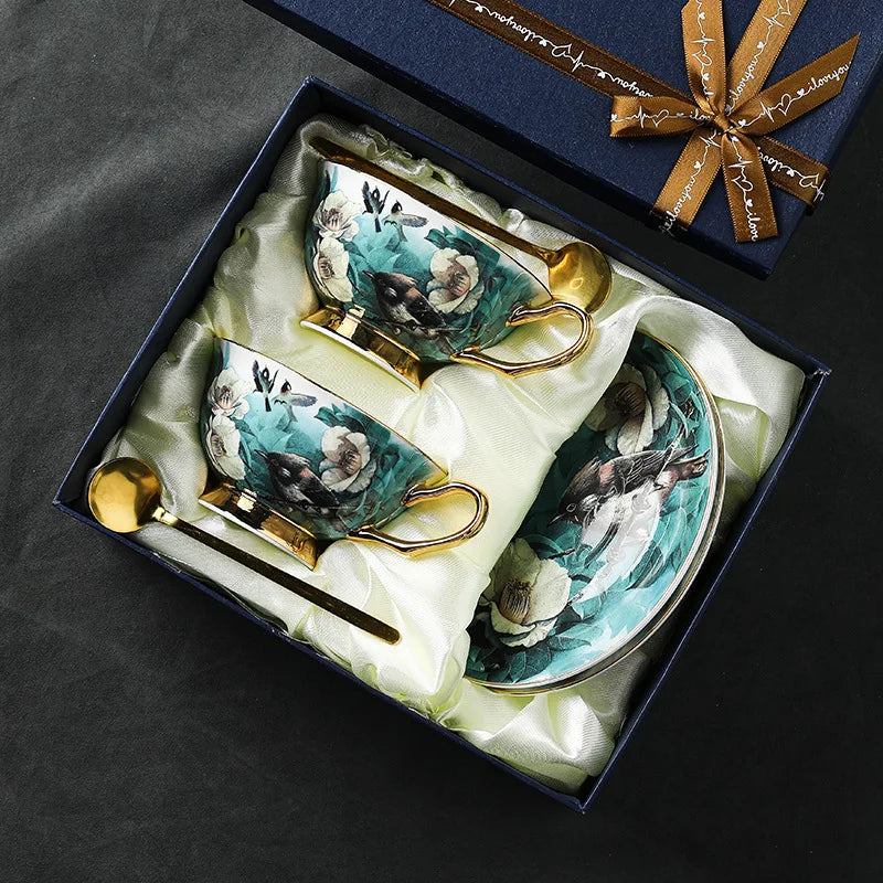 Tea set with decorative teacups, saucer, and spoon in a gift box on a dark surface.