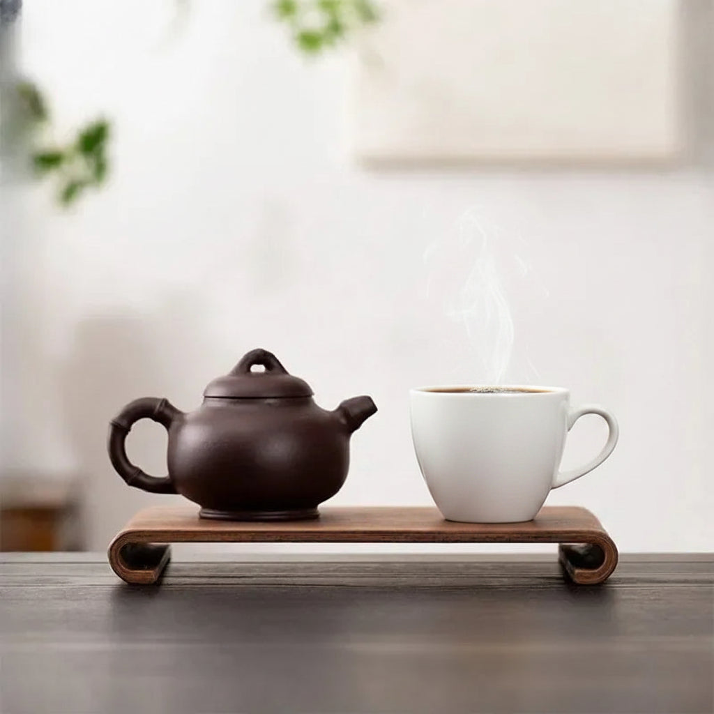 Tea pot and glass with tea on a wooden tray against a blurred background