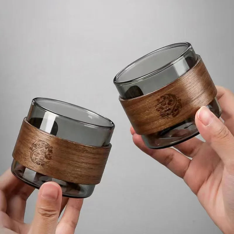 Two glass containers with wooden wraps held by hands against a gray background
