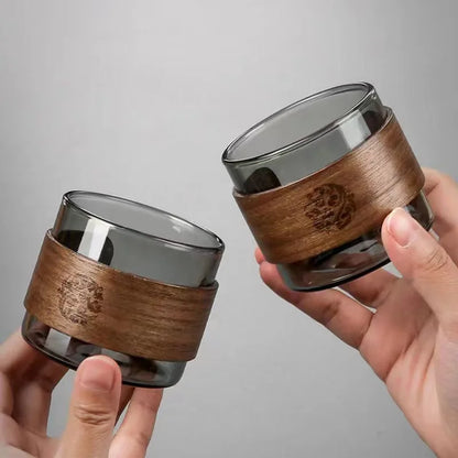 Two glass containers with wooden wraps held by hands against a gray background