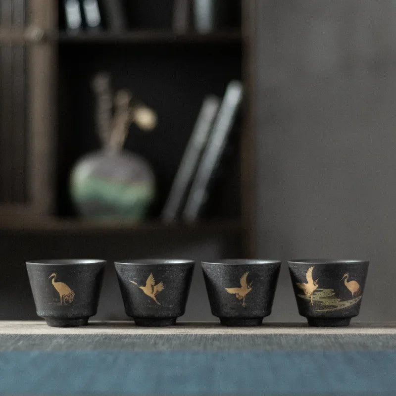 Four black ceramic cups with bird illustrations on a wooden surface.