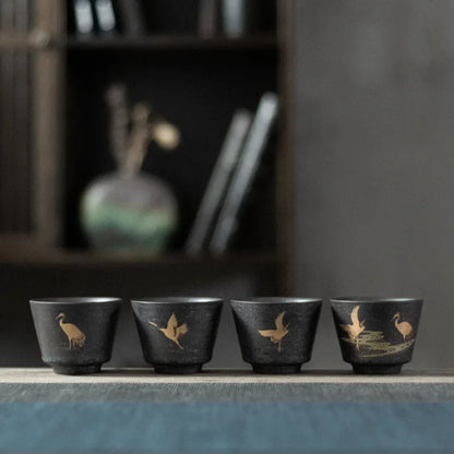 Four black ceramic cups with bird illustrations on a wooden surface.