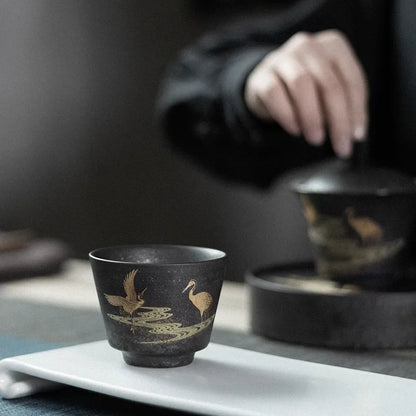 Black ceramic cup with gold bird design on a white tray, blurred background