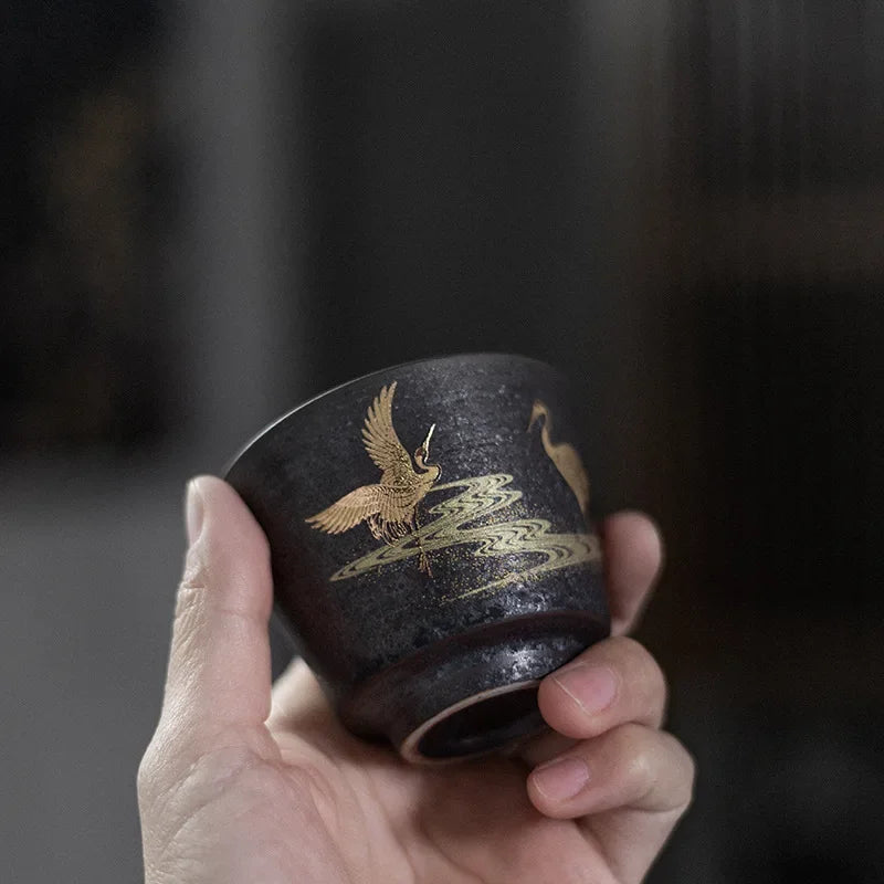 Hand holding a black ceramic cup with gold eagle design against a dark background