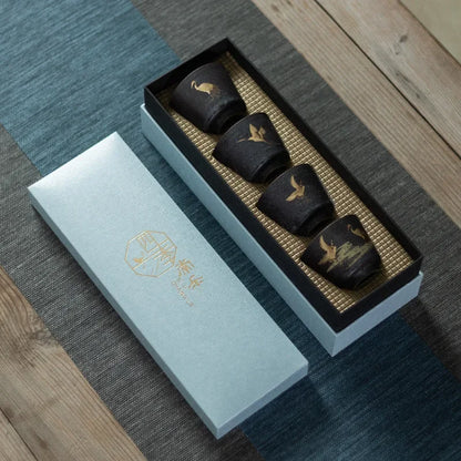 Set of black ceramic cups with gold accents in a decorative box on a wooden surface.