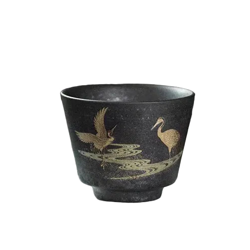Black ceramic cup with gold bird design on a white tray, blurred background