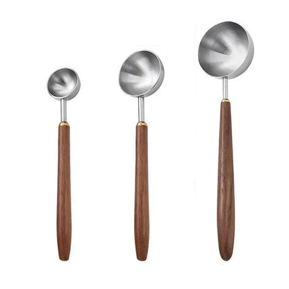 Three metal measuring spoons with wooden handles shown on a white background.