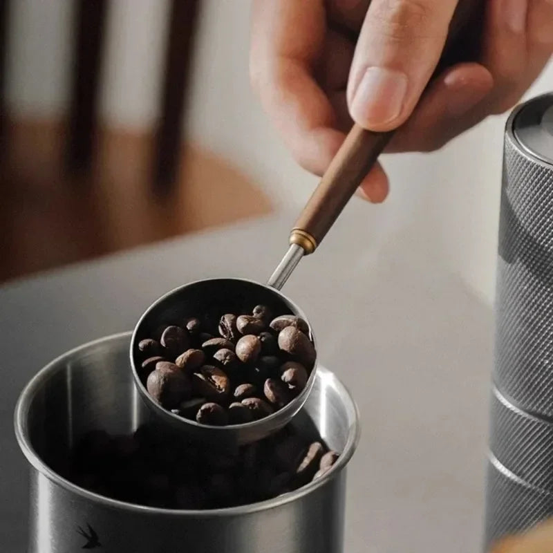 Hand using a coffee scoop to measure coffee beans into a container.