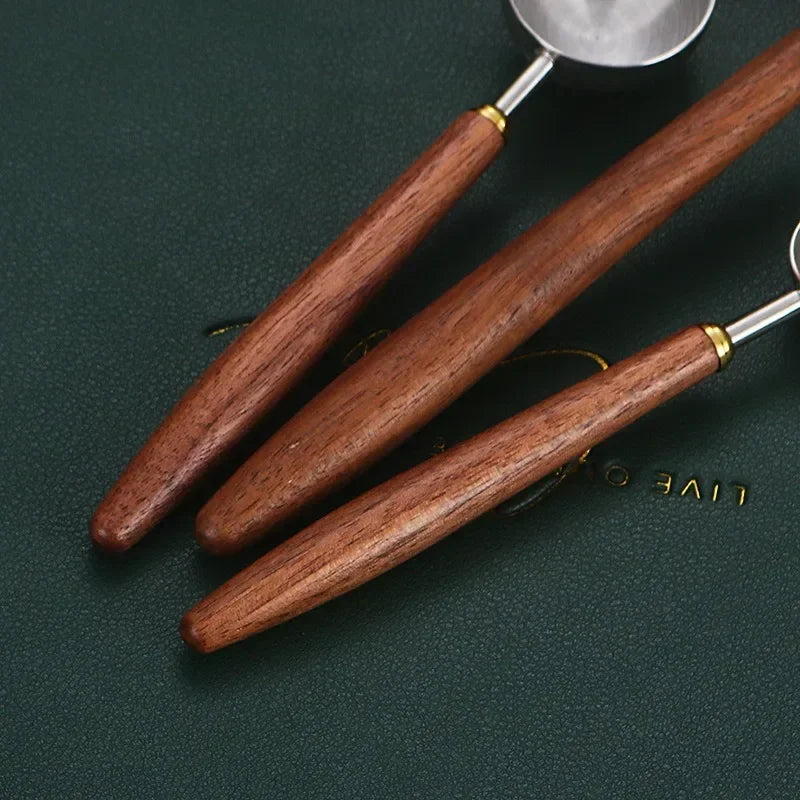 Three wooden-handled kitchen utensils with silver metal heads, arranged diagonally on a dark green textured background.