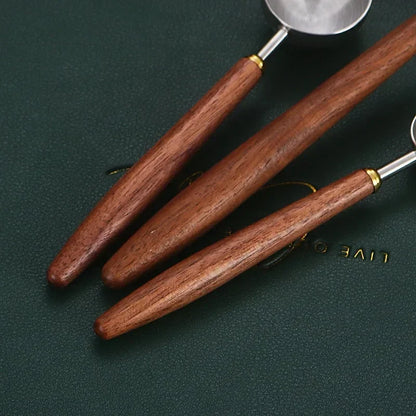 Three wooden-handled kitchen utensils with silver metal heads, arranged diagonally on a dark green textured background.