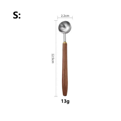 A small metal spoon with a brown wooden handle and a gold-toned ferrule, shown on a white background with dimension labels indicating 2.2 cm bowl diameter, 12.