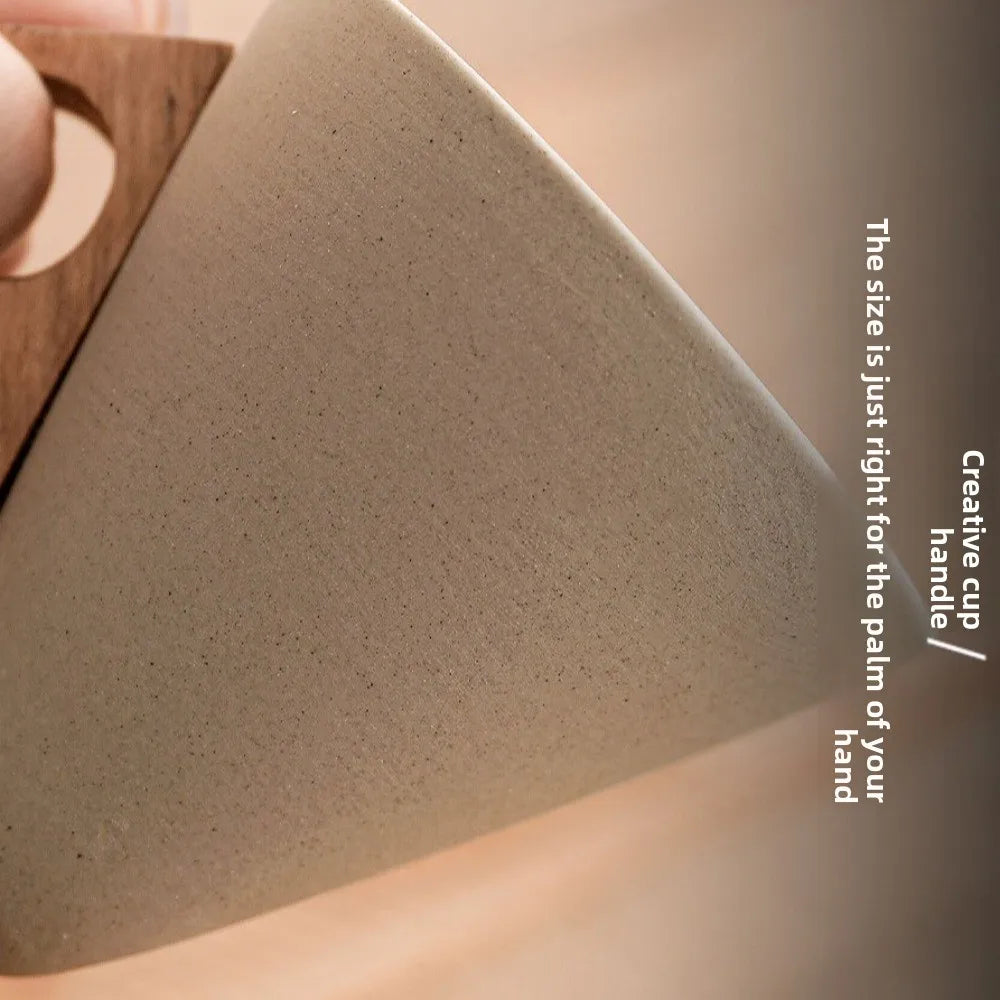 Close-up of a textured ceramic cup with a wooden handle held by a hand.