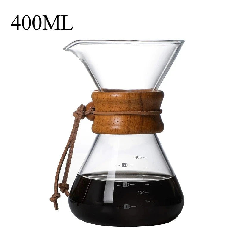 Clear glass coffee maker with wooden collar and brown tie, filled with coffee, on a white background.