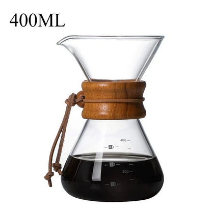 Clear glass coffee maker with wooden collar and brown tie, filled with coffee, on a white background.