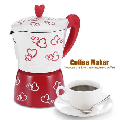 Red and white coffee maker with heart designs next to a cup of coffee on a white background