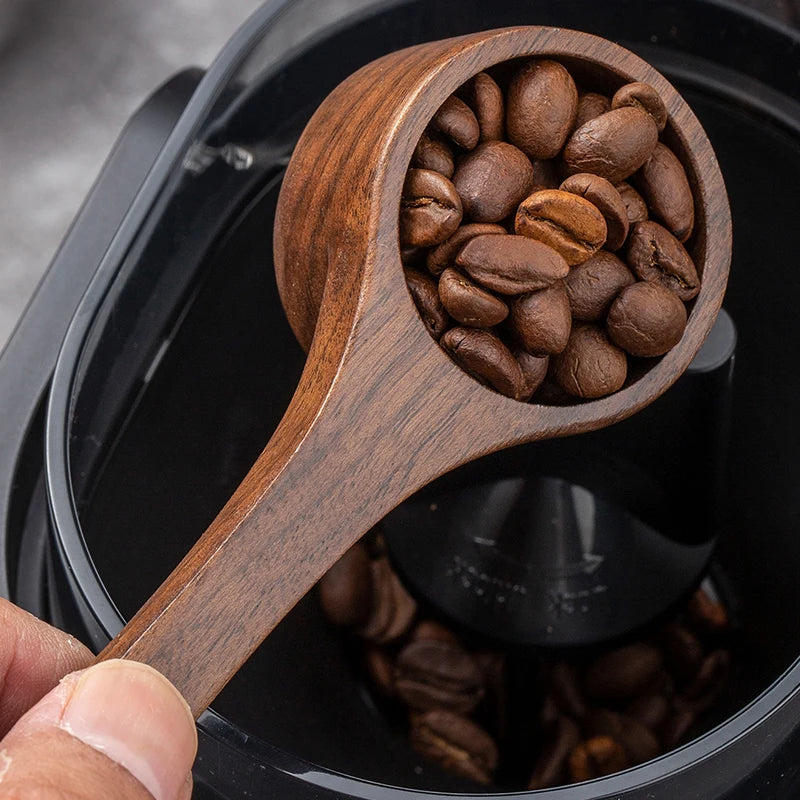Wooden scoop filled with coffee beans held over a coffee grinder.